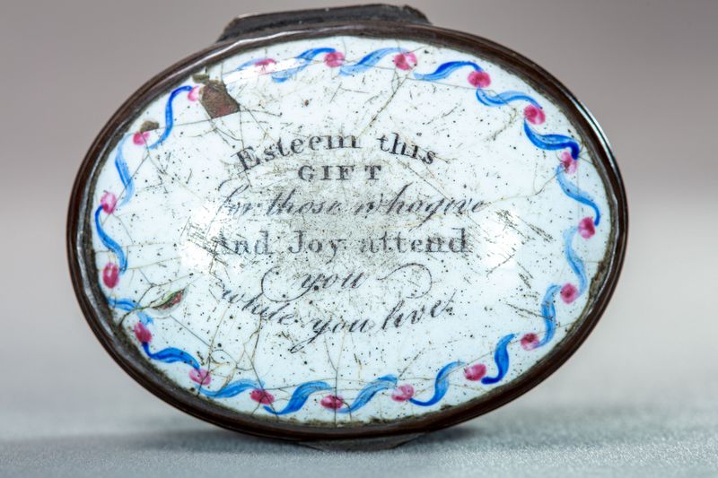 White, oval enamel box with a blue and rd decorative border and the motto in the centre