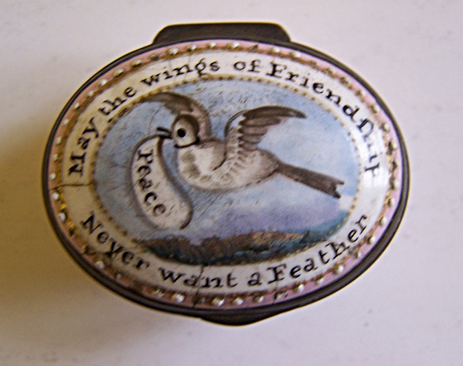 An enamel box with a pink and white border and the motto running around the edge; in the centre, a white bird flies in a blue sky with a speech bubble saying, 'Peace'