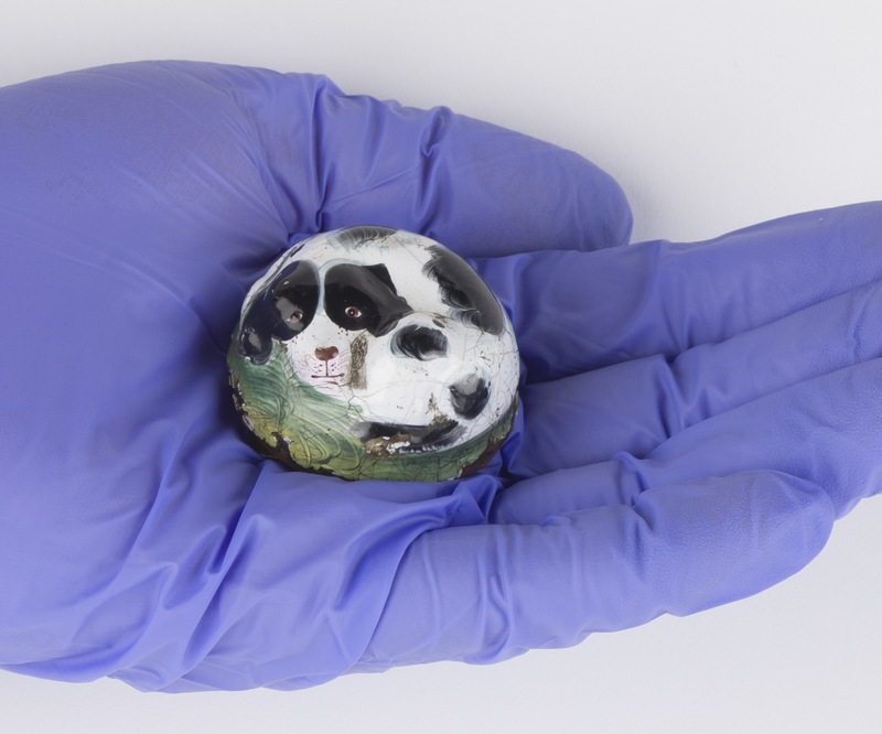 Small, dog-shaped patch box held in a gloved hand