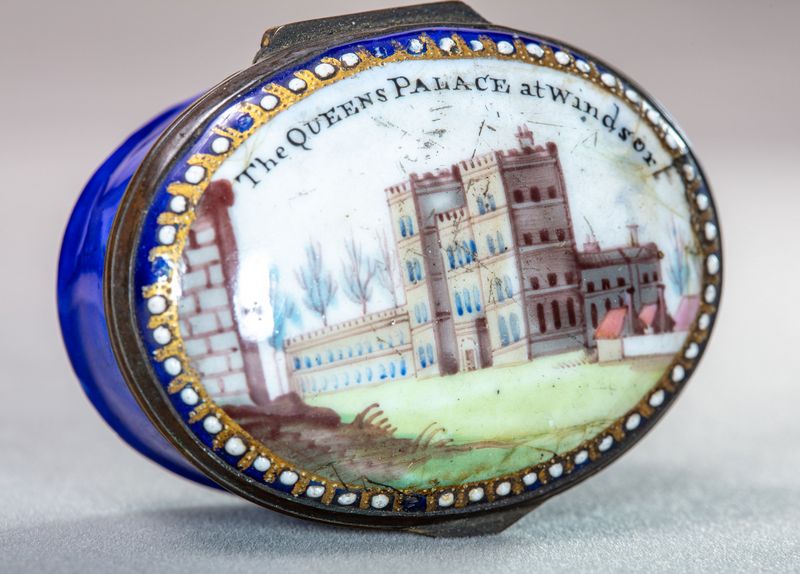 Bright blue patch box with gold and white dotted decoration around the lid, which has a colourful painting of a castle with lots of windows and another wall jutting into the foreground from the left