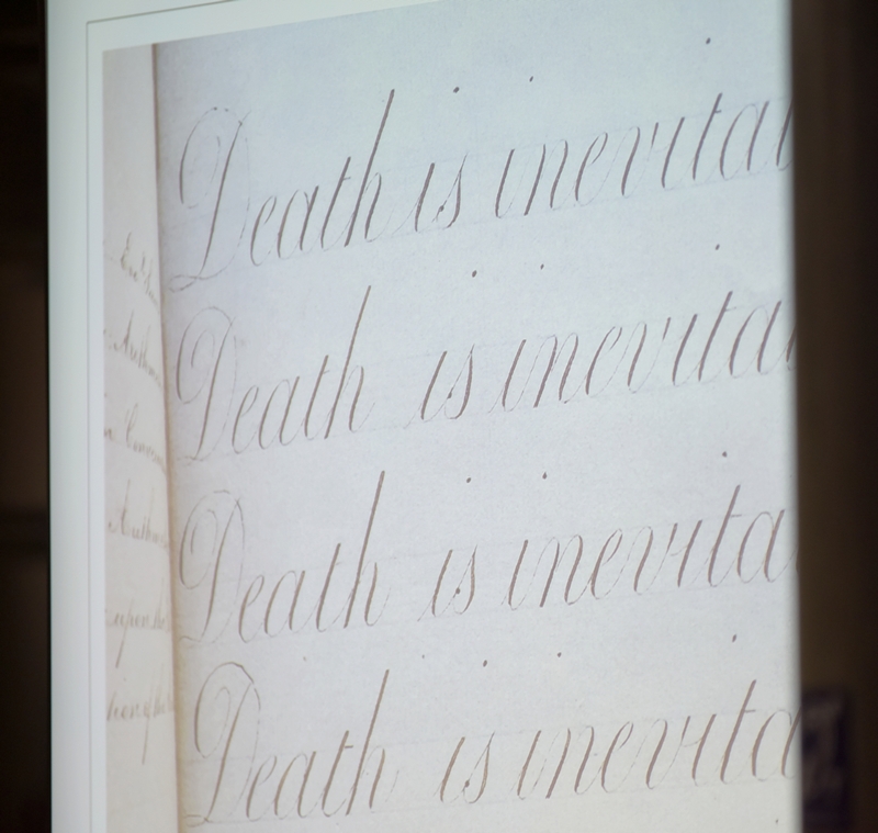 The page of a child's copy book with the line 'Death is inevita[ble] over and over in copperplate